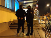 Na zdjęciu widać umundurowanego policjanta, który trzyma mężczyznę z kajdankami założonymi na ręce trzymane z tyłu. Obydwaj są odwróceni tyłem i stoją na schodach przed drzwiami wejściowymi do komisariatu w Karczewie.
