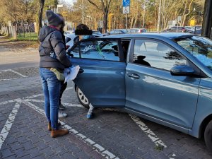 Na zdjęciu jest nieoznakowany radiowóz, którego tylne drzwi są otwarte. Przy drzwiach widać dwóch nieumundurowanych policjantów oraz wsiadającego do samochodu mężczyznę.
