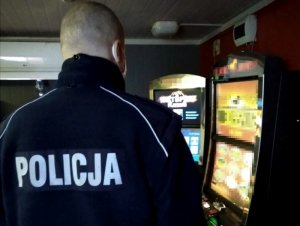 Na zdjęciu widać odwróconego tyłem policjanta, który stoi przed automatami do gier.