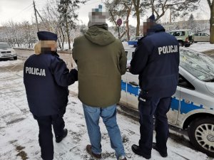 Na zdjęciu widać umundurowanych policjantów, którzy prowadzą zatrzymanego mężczyznę.