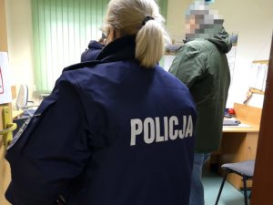 Na zdjęciu widać umundurowaną policjantkę, która stoi w otwartych drzwiach pokoju służbowego. Wewnątrz pokoju stoi mężczyzna.