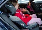 Na zdjęciu widać dziecko posadzone w foteliku samochodu, który jest zamontowany wewnątrz pojazdu.