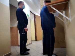 Na zdjęciu widać umundurowanego policjanta, który wprowadza mężczyznę do celi.