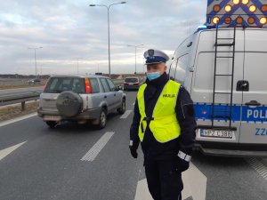 Na zdjęciu widać umundurowanego policjanta drogówki, który stoi przed oznakowanym radiowozem.
