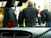 Zdjęcie jest zrobione przez przednią szybę pojazdu. Przed pojazdem stoją dwaj odwróceni tyłem nieumundurowani policjanci.