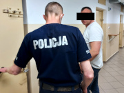 Na zdjęciu widać stojącego tyłem do zdjęcia umundurowanego policjanta, który trzyma zamknięte drzwi do policyjnej celi. Przed funkcjonariuszem stoi mężczyzna.