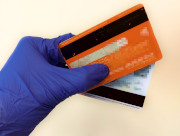 Na zdjęciu widać rękę w rękawiczce lateksowej koloru niebieskiego, która trzyma dwie karty płatnicze.