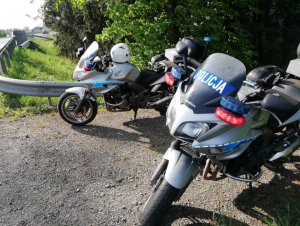 Na zdjęciu widać dwa zaparkowane obok siebie, na poboczu drogi policyjne motocykle.