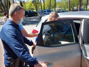 Na zdjęciu widać dwóch nieumundurowanych policjantów, którzy stoją przy radiowozie, i mężczyznę, który wsiada do radiowozu.