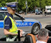 Na zdjęciu widać umundurowaną policjantkę z wydziału ruchu drogowego, która przeprowadza badanie stanu trzeźwości mężczyzny siedzącego za kółkiem pojazdu osobowego.