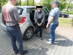 Na zdjęciu widać dwóch nieumundurowanych policjantów, którzy stoją obok nieoznakowanego radiowozu koloru szarego. Z pojazdu wysiada mężczyzna.