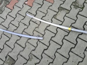 Na zdjęciu widać miecz koloru szarego ułożony na chodniku z kostki brukowej.