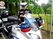 Na zdjęciu widać zaparkowany przy ulicy policyjny motocykl. Obok jednośladu stoi umundurowany policjant z drogówki.