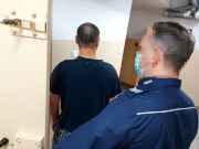 Na zdjęciu widać umundurowanego policjanta, który trzyma otwarte drzwi do policyjnej celi. Przed policjantem stoi mężczyzna. Obaj są odwróceni tyłem do zdjęcia.