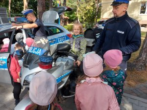 Na zdjęciu widać chłopca siedzącego na policyjnym motocyklu. Obok motocyklu stoją umundurowani policjanci i przedszkolaki.