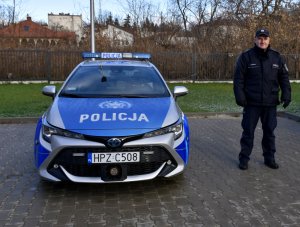 Na zdjęciu widać oznakowany radiowóz obok którego stoi umundurowany policjant.