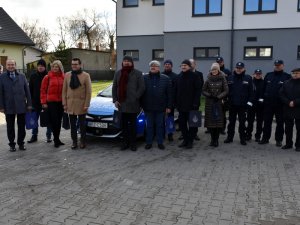 Na zdjęciu widać przedstawicieli samorządów z powiatu otwockiego i kadrę kierowniczą otwockiej komendy ustawionych przed oznakowanym radiowozem do zdjęcia. Wszyscy stoją przodem do zdjęcia.