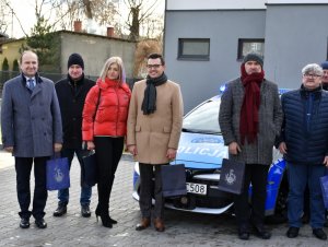 Na zdjęciu widać przedstawicieli samorządów z powiatu otwockiego ustawiony przy oznakowanym radiowozie. Wszyscy są odwróceni przodem do zdjęcia.
