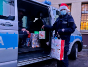 Na zdjęciu widać umundurowaną policjantkę z czapką Mikołaja, która trzyma paczki i pakuje je do oznakowanego radiowozu.