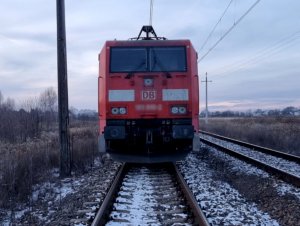 Na zdjęciu widać stojący na torach pociąg koloru czerwonego.Zdjęcie jest zrobione z przodu lokomotywy.