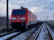Na zdjęciu widać stojący na torach pociąg koloru czerwonego. Zdjęcie jest wykonane z lewej strony lokomotywy.