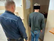 Na zdjęciu widać umundurowanego policjanta, który trzyma otwarte drzwi do policyjnej celi. Przed nim stoi mężczyzna, który wchodzi do pomieszczenia.