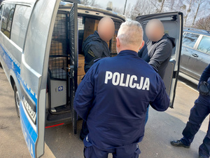Na zdjęciu widać umundurowanych policjantów, którzy pakują kartony do oznakowanego radiowozu typu bus.