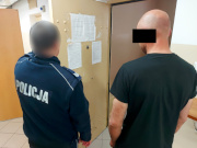 Na zdjęciu widać umundurowanego policjanta z mężczyzną. Obaj są odwróceni tyłem do zdjęcia. Zdjęcie jest wykonane przed drzwiami policyjnej celi.