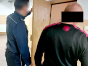 Na zdjęciu jest umundurowany policjant, który trzyma otwarte drzwi do policyjnej celi. Obok niego stoi mężczyzna. Obaj są odwróceni tyłem do zdjęcia.