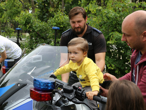 Na zdjęciu widać chłopca siedzącego na policyjnym motocyklu. W tle jest umundurowany policjant.