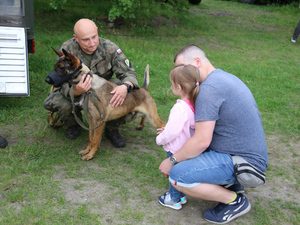 Żołnierz z psem służbowym i zainteresowani uczestnicy pikniku.