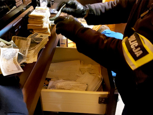 Na zdjęciu widać nieumundurowanego policjanta, który wyciąga z szuflady gotówkę w banknotach o różnych nominałach.